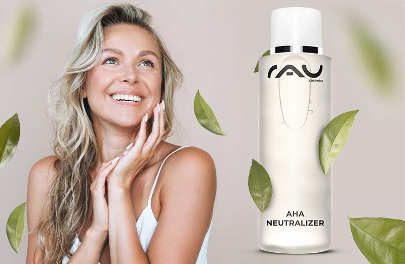 Frau mit strahlendem Lächeln und AHA Neutralizer von RAU Cosmetics, umgeben von dekorativen grünen Blättern.