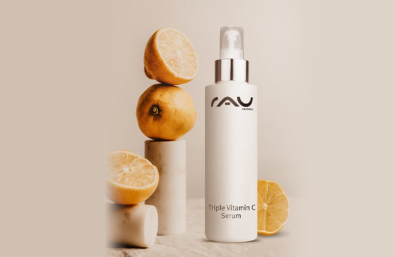 Flasche mit RAU Triple Vitamin C Serum, umgeben von frischen Zitronen, auf neutralem Hintergrund, betont die Vorteile von Vitamin C für die Hautpflege im Sommer.