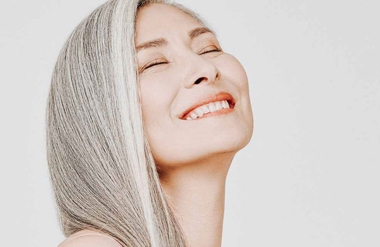 Le secret anti-âge venu d'Asie : le thé blanc ! Lächelnde Frau mit grauen Haaren und strahlender Haut, repräsentiert die Anti-Aging-Vorteile von Hautpflegeprodukten mit weißem Tee.