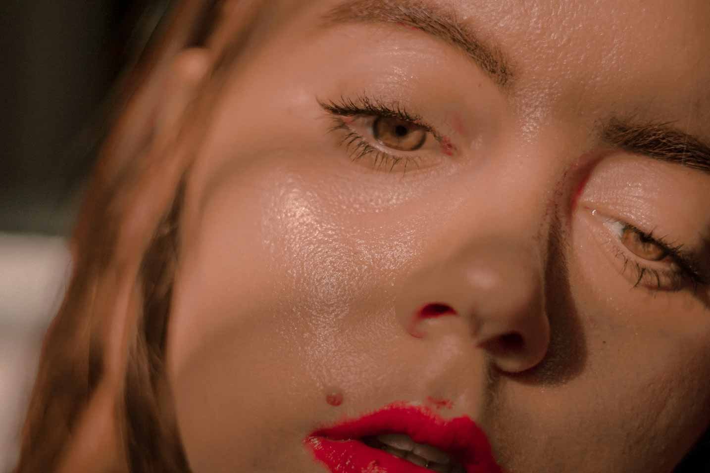 Nahaufnahme eines Gesichts mit glänzender Haut und roten Lippen, passend zu Tipps zur Gesichtspflege und Schweißbewältigung im Sommer.