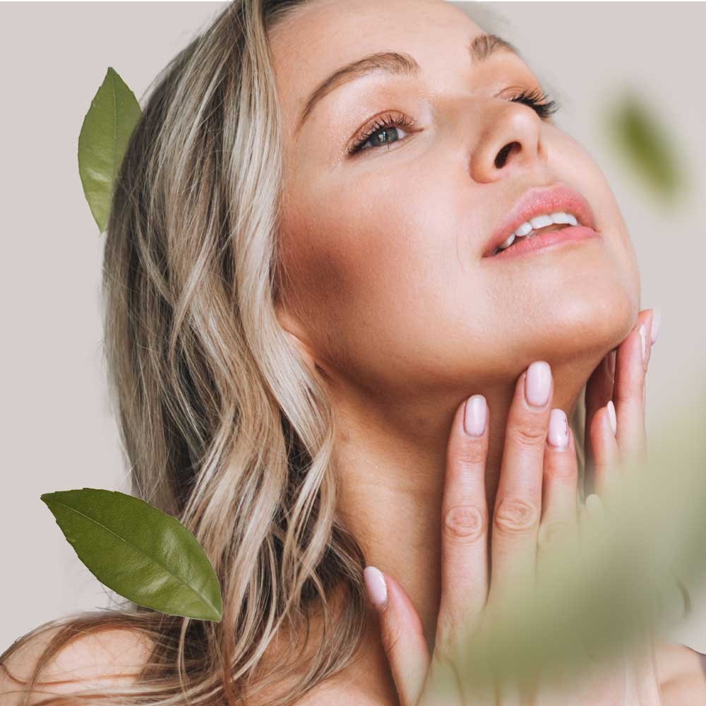 Frau mit blonden Haaren, die sanft ihren Hals berührt, umgeben von grünen Blättern, symbolisiert hochwertige Hautpflege und natürliche Inhaltsstoffe von RAU Cosmetics.