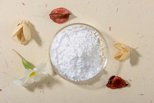 allantoin-wirkstoff-urea-empfindliche-trockene-haut-rau-cosmetics Pulverförmiger Allantoin in einer Glasschale, umgeben von getrockneten Blüten und Pflanzenmaterialien, symbolisiert die natürlichen Inhaltsstoffe in Hautpflegeprodukten.