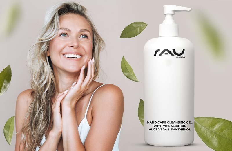 Frau mit welligem Haar, lächelnd, präsentiert RAU Cosmetics 500 ml Handreinigungsgel mit 70% Alkohol und Aloe Vera.