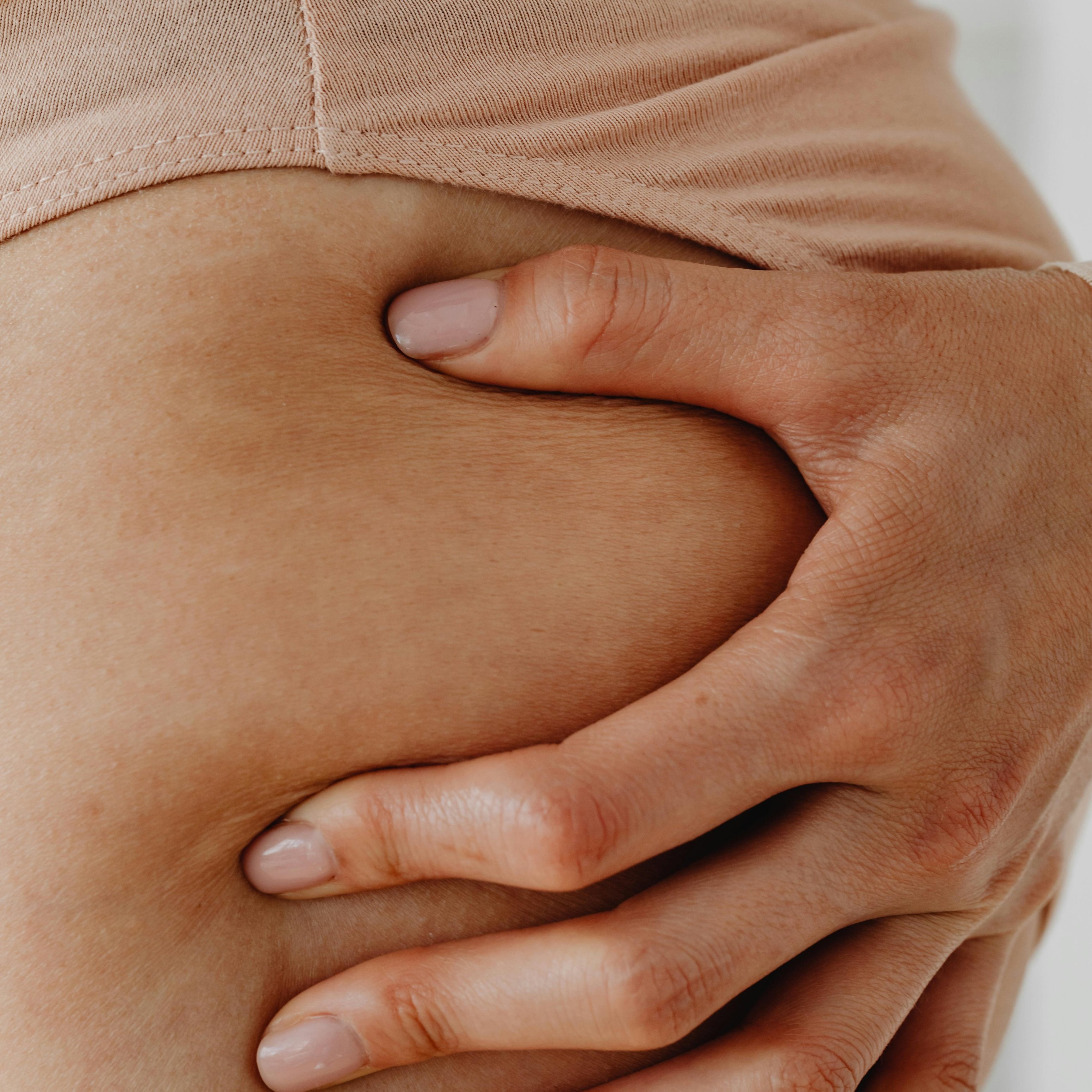 Hautbereich mit Dehnungsstreifen, Hand, die sanft auf die Haut drückt, Bezug zu Hautpflege und Dehnungsstreifenbehandlung.