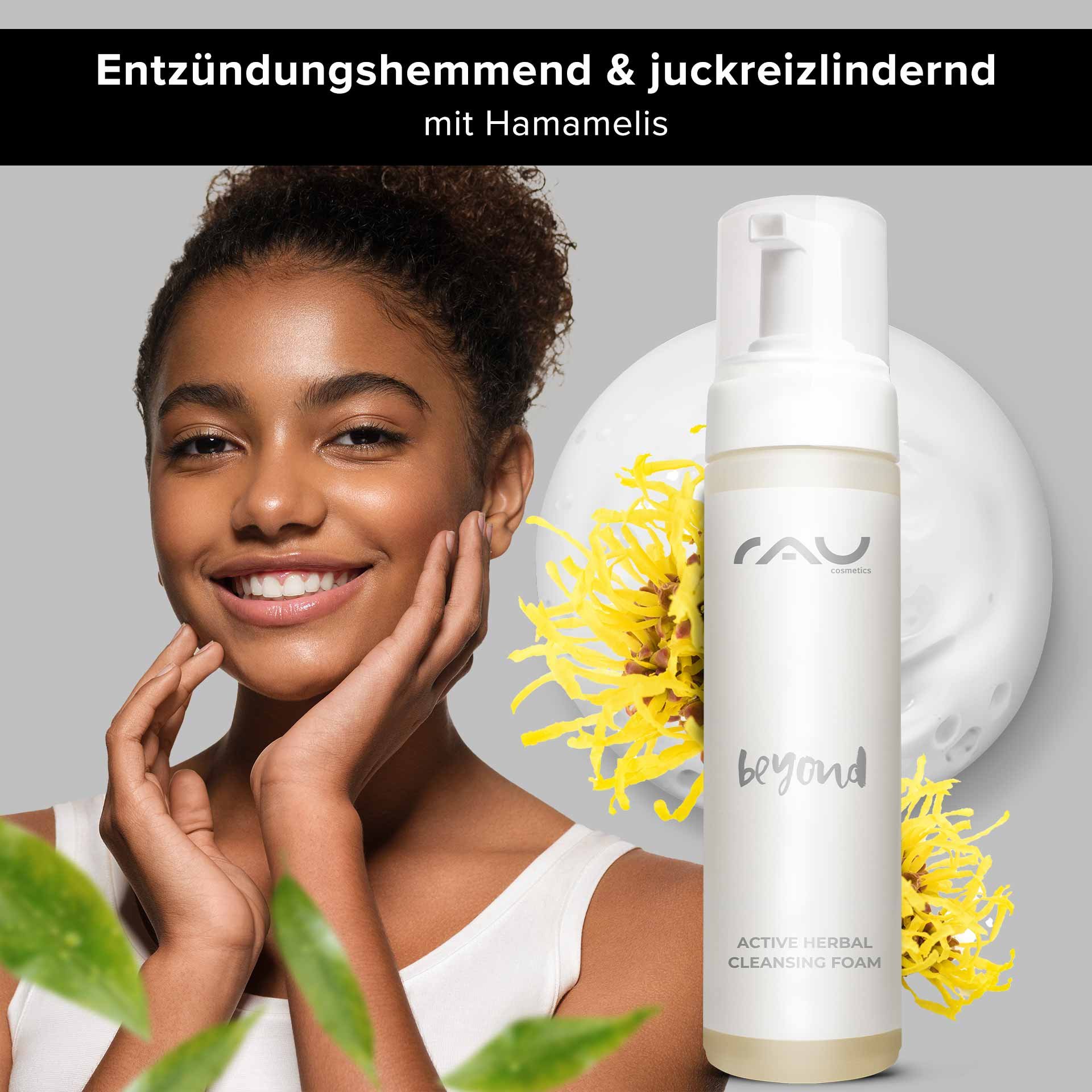 Lächelnde Frau mit glatter Haut, die RAU Cosmetics Active Herbal Cleansing Foam präsentiert, umgeben von Hamamelisblüten und grünen Blättern, betont die entzündungshemmenden Eigenschaften des Gesichtsreinigers.